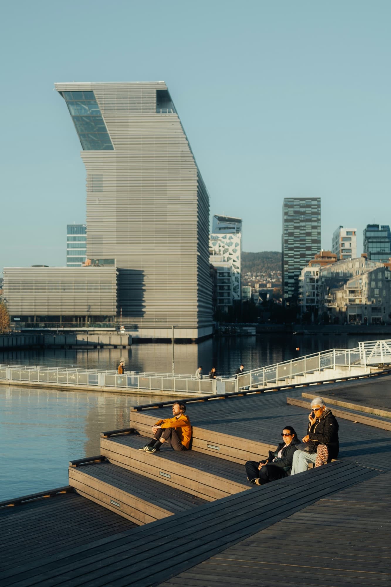 Folk på trappene ved fjorden i Bjørvika i Oslo, med nye boligblokker bak